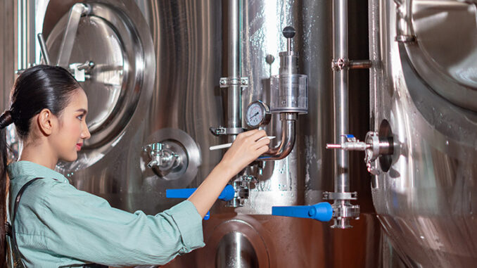 A woman adjusts equipment in a brewery showcasing the brewing pr